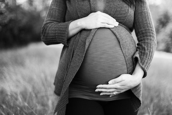 Femme enceinte entourant son ventre de ses mains dans la nature en noir et blanc