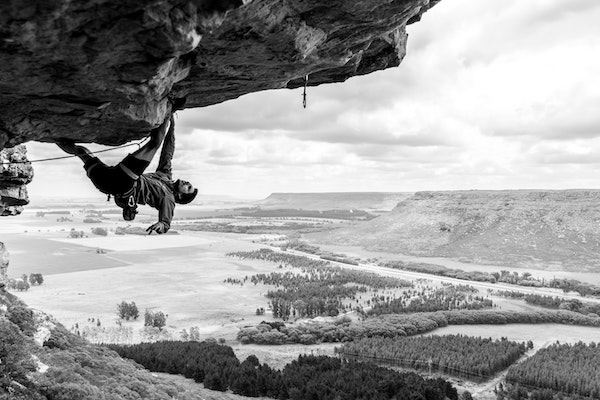 Grimpeur en mouvement sur une falaise avec panorama de champs et de montagnes en noir et blanc